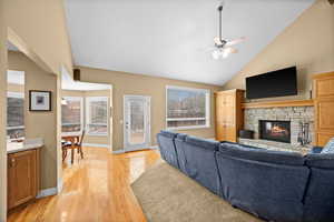 Living room featuring ceiling fan, lofted ceiling, a fireplace, and light wood-type flooring