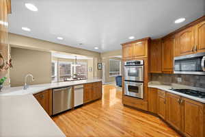 Kitchen featuring sink, hanging light fixtures, light wood-type flooring, appliances with stainless steel finishes, and decorative backsplash