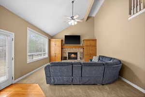 Living room with high vaulted ceiling, a stone fireplace, light colored carpet, and ceiling fan