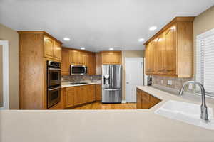 Kitchen with stainless steel appliances, sink, light hardwood / wood-style flooring, and decorative backsplash