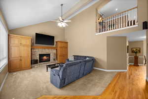 Carpeted living room featuring ceiling fan, a stone fireplace, and high vaulted ceiling