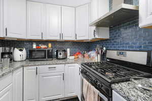 Kitchen with tasteful backsplash, wall chimney range hood, white cabinets, and appliances with stainless steel finishes