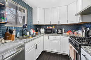 Kitchen featuring stainless steel appliances, sink, wall chimney range hood, and white cabinets