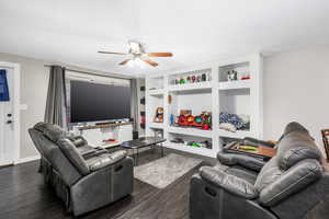 Living room with built in shelves, dark hardwood / wood-style floors, and ceiling fan