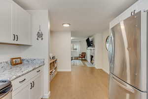 Kitchen with stainless steel refrigerator, white cabinets, range, light stone counters, and light hardwood / wood-style flooring