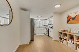 Kitchen with stainless steel appliances, sink, light hardwood / wood-style flooring, and white cabinets