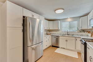 Kitchen with sink, light stone counters, light hardwood / wood-style flooring, stainless steel appliances, and white cabinets