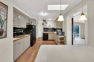 Kitchen featuring hanging light fixtures, a skylight, decorative backsplash, and black appliances