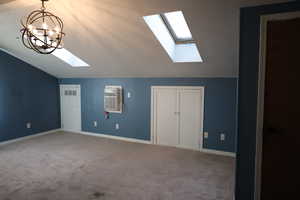 Interior space featuring a chandelier, vaulted ceiling with skylight, a wall mounted AC, and light carpet