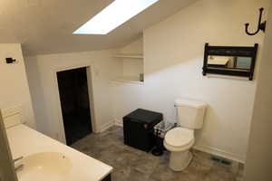 Bathroom with vanity, toilet, and lofted ceiling with skylight