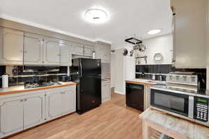 Kitchen featuring sink, tasteful backsplash, ornamental molding, light hardwood / wood-style floors, and black appliances