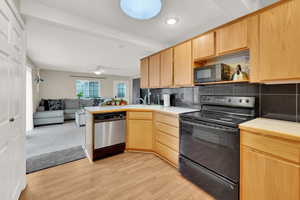 Kitchen featuring backsplash, black appliances, light brown cabinets, kitchen peninsula, and light wood-type flooring