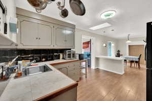 Kitchen with sink, hanging light fixtures, a skylight, light hardwood / wood-style floors, and decorative backsplash