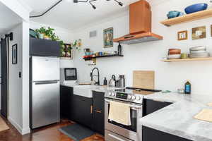 Kitchen featuring appliances with stainless steel finishes, range hood, sink, light stone counters, and crown molding