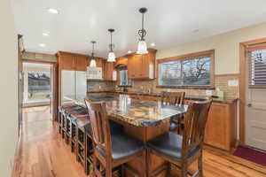 Kitchen featuring a breakfast bar, stone countertops, white appliances, and decorative light fixtures.