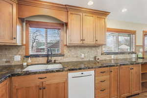 Kitchen with backsplash, white dishwasher, sink, and stone countertops.