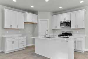 Kitchen with a kitchen island with sink, stainless steel appliances, and white cabinets
