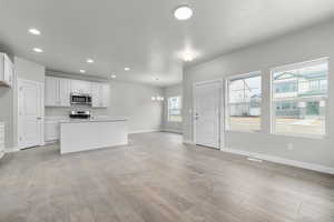 Kitchen featuring white cabinetry, stainless steel appliances, decorative light fixtures, and light hardwood / wood-style flooring