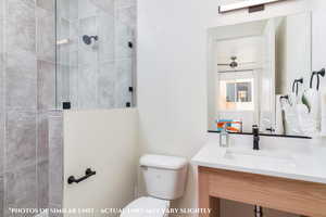 Bathroom featuring tiled shower, vanity, and toilet