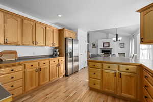 Kitchen featuring vaulted ceiling, decorative light fixtures, a notable chandelier, stainless steel fridge with ice dispenser, and light hardwood / wood-style flooring