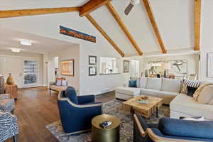 Living room with dark wood-type flooring, ceiling fan, high vaulted ceiling, and beamed ceiling