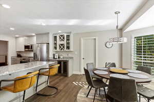 Kitchen featuring dark hardwood / wood-style floors, white cabinetry, hanging light fixtures, light stone counters, and stainless steel appliances