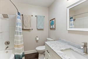 Full bathroom with hardwood / wood-style floors, vanity, shower / bath combination with curtain, a textured ceiling, and toilet