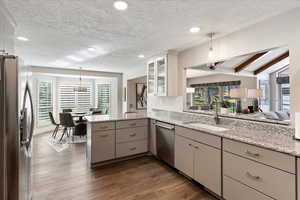 Kitchen with decorative light fixtures, sink, kitchen peninsula, stainless steel appliances, and light stone countertops