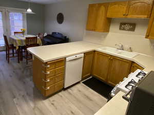 Kitchen featuring decorative light fixtures, sink, light hardwood / wood-style floors, kitchen peninsula, and white appliances