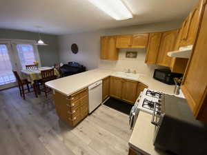 Kitchen featuring sink, light hardwood / wood-style flooring, kitchen peninsula, pendant lighting, and white appliances