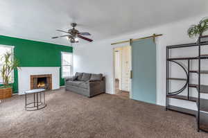 Carpeted living room with a barn door, ceiling fan, and a brick fireplace