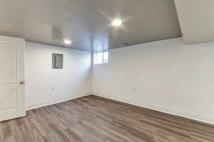 Basement with hardwood / wood-style flooring, electric panel, and a textured ceiling