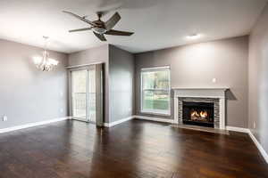 Unfurnished living room featuring dark wood-type flooring, a stone fireplace, and ceiling fan with notable chandelier