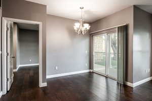 Spare room with a notable chandelier and dark hardwood / wood-style floors