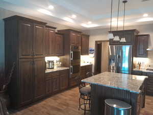 Kitchen with stainless steel appliances, a center island, wood-type flooring, and dark brown cabinets