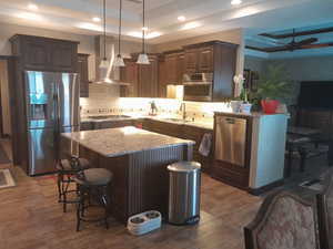 Kitchen with stainless steel appliances, a raised ceiling, a kitchen island, and wall chimney range hood