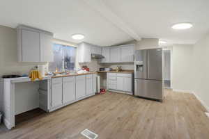 Kitchen featuring stainless steel fridge, white cabinetry, backsplash, light hardwood / wood-style floors, and lofted ceiling with beams