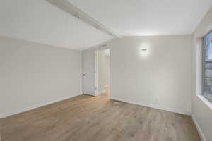 Unfurnished room with lofted ceiling with beams, plenty of natural light, and light wood-type flooring