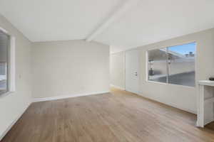 Empty room with lofted ceiling with beams and light wood-type flooring