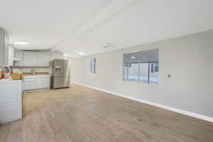 Kitchen featuring lofted ceiling with beams, white cabinetry, decorative backsplash, light hardwood / wood-style floors, and stainless steel refrigerator with ice dispenser