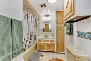 Full bathroom featuring tasteful backsplash, shower / bath combination with curtain, tile patterned flooring, vanity, and toilet