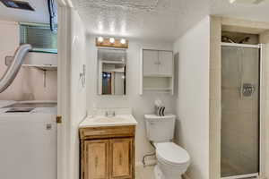 Bathroom with washer / clothes dryer, vanity, toilet, a shower with door, and a textured ceiling