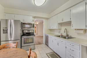 Kitchen with appliances with stainless steel finishes, sink, light tile patterned floors, and white cabinets