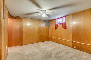 Unfurnished room featuring ceiling fan, light colored carpet, and wooden walls