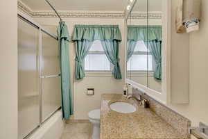 Full bathroom featuring toilet, vanity, shower / bath combination with glass door, and tile patterned flooring