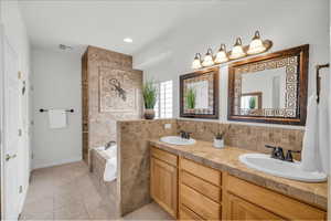 Bathroom featuring a relaxing tiled tub, decorative backsplash, tile patterned floors, and vanity