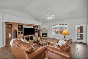 Living room with lofted ceiling, light tile patterned floors, a fireplace, and ceiling fan