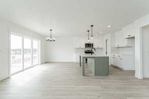 Kitchen with decorative backsplash, a chandelier, stainless steel microwave, light countertops, and a sink