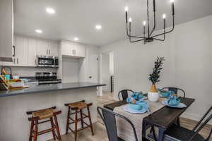 Kitchen with a breakfast bar area, light hardwood / wood-style flooring, appliances with stainless steel finishes, kitchen peninsula, and white cabinets