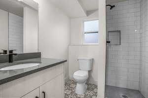 Bathroom featuring tile patterned flooring, vanity, a tile shower, a textured ceiling, and toilet